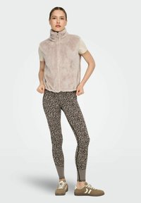 Udune beež varrukateta vest kõrge kraega, kombineeritud sobivate, mustriliste pruunide retuusidega, millel on peened lillemustrid ja võrgusilmadetailid. Pruunid tossud.