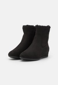 Bottines chevilles en suédine noire avec fermeture éclair, doublure douce en fausse fourrure, bout arrondi et petit talon compensé pour le confort.