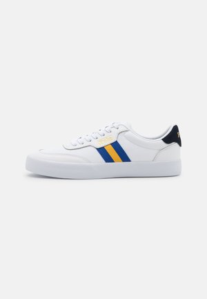 Weißer Sneaker mit niedrigem Schaft, blauen und gelben seitlichen Streifen, weißen Schnürsenkeln und einer marineblauen Fersenlasche auf einem schlichten hellen Hintergrund.