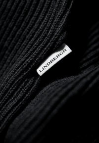 Tessuto a maglia nero con texture a coste, con un'etichetta bianca che mostra "LINDBERGH" attaccata al bordo.