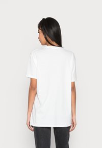 T-shirt branca de algodão com decote redondo e mangas curtas, apresentando um corte confortável. A vista traseira revela uma textura suave e um design simples.