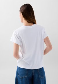 T-shirt bianco a maniche corte con scollo rotondo, tessuto morbido, vestibilità rilassata e orlo posteriore dritto, abbinato a pantaloni in denim blu.