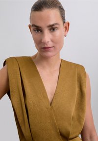 Senfgelbes, ärmelloses Wickeloberteil mit tiefem V-Ausschnitt und strukturiertem Stoff, der Drapierungen um die Schultern aufweist.