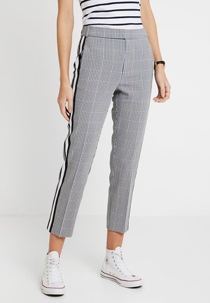 Pantaloni a quadri bianchi e neri con gamba affusolata, strisce laterali e vita alta, realizzati in un tessuto liscio, abbinati a sneakers bianche.