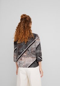 Blusa stampata a serpente in bianco e nero con maniche a tre quarti, caratterizzata da strisce diagonali e una trama liscia. Pantaloni bianchi semplici sotto.