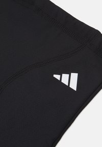 Schwarze Sportshorts mit glatter Textur, ausgestattet mit einem weißen Logo und Nahtdetails an der Seite.