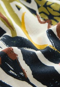 Tissu multicolore avec des motifs abstraits en noir, jaune et vert sur fond crème ; texture douce, apparence légèrement froissée.