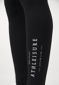 Black athleisure leggings featuring a fitted design, soft texture, and white printed text along the left leg, highlighting the brand name and slogan.