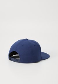 Tamsiai mėlynas medvilninis beisbolo kepurėlė su plokščiu kraštu, reguliuojama snapback uždanga ir ventiliacijos skylutėmis ant galinės panelės.