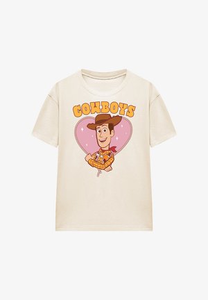 Beige T-shirt with cartoon cowboy wearing a hat and checked shirt inside a heart-shaped rope design, text "COWBOYS" above.