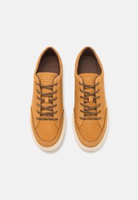 Baskets en cuir tan avec des lacets marron, des détails perforés et une semelle en caoutchouc crème. Présente un logo embossé sur la languette.