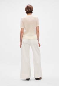 Krémový sveter s krátkym rukávom a jemnou textúrou, kombinovaný s bielymi širokými nohavicami so zadnými vreckami a manžetami.