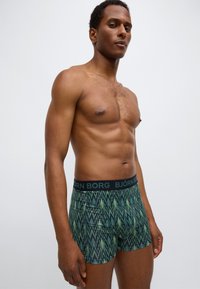 Pánské boxerky se zeleno-černým cikcak vzorem. Vyrobené z elastické látky s černým páskem s logem značky.
