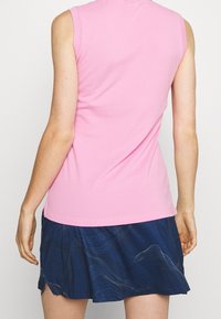 Różowy top bez rękawów wykonany z gładkiej tkaniny, zestawiony z ciemnoniebieską spódnicą z falistym wzorem, tworzący warstwowy efekt.