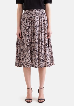 Kvinde iført en pink midi nederdel med sort blomsterprint, sort top med korte ærmer og sorte højhælede sandaler med ankelrem.