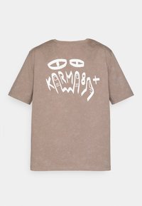 Brown cotton t-shirt with a relaxed fit, featuring a large white graphic design with eyes and stylized text "KARMA" on the back.