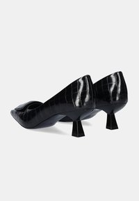 Zapatos de charol negro con textura de cocodrilo, punta afilada y un diseño único de tacón ancho. Los zapatos presentan un detalle de corte distintivo.