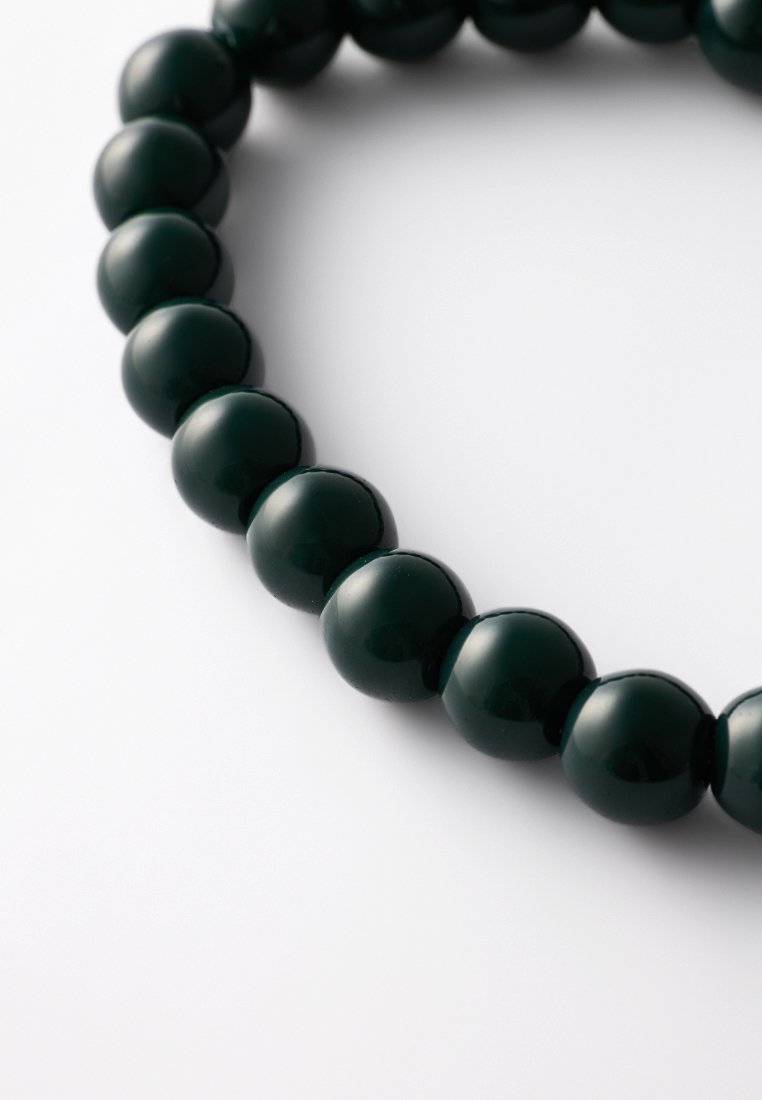 Perles rondes brillantes de couleur vert foncé, serrées les unes contre les autres, formant un cercle partiel sur une surface blanche.