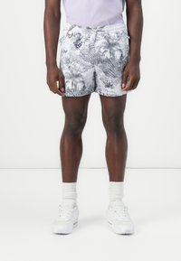 Swim shorts with a gray and black tropical pattern, elastic waistband, and side pockets, paired with white sneakers and crew socks.