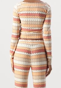 Ribstrikket to-delt sæt med geometrisk mønster i varme nuancer af orange, rød og beige. Lange ærmer og tætsiddende silhuet.