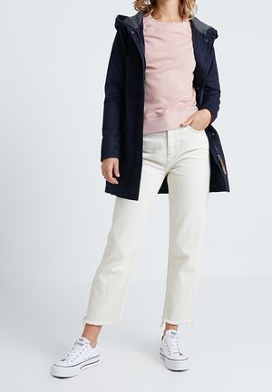 Marinblå vattentät kappa med grå huva, ljusrosa sweatshirt, vita korta jeans och vita sneakers med en avslappnad design och fransiga kanter.