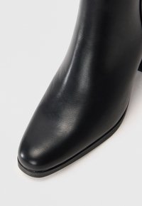 Sorte skinn ankle boots med spiss tå, glatt overflate og lav, stablet hæl. Designet er slankt og minimalistisk.