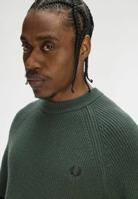 Maglione verde a maglia con trama e scollo rotondo con dettagli a coste. Presenta un piccolo logo ricamato sul petto.