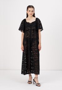 Black lace dress with short, flared sleeves and a button front. The fabric is sheer, featuring a floral pattern, and falls to mid-calf.