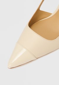 Beige värinen nahkainen slingback-avokärkikorkokenkä. Kiiltävä lakattu kärki ja sileä matta runko. Avoimet sivut ja hienovaraiset ompelukoristeet.