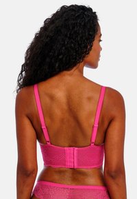 Růžová krajková podprsenka se zapínáním na zádech a dekorativním lemem podél okrajů. Hladký materiál s květinovým vzorem.