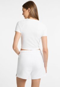 Bijeli crop top s kratkim rukavima uparen s bijelim šortsevima. Oboje imaju glatku teksturu, dizajnirano za udobnost i ležerno nošenje.