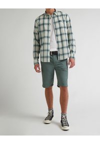 Kostkovaná košile na knoflíky v tónech teal, bílé a námořnické, doplněná o zelené šortky. Černé vysoké tenisky, šedé ponožky a černý opasek dokončují celkový vzhled.