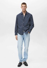 Marineblå stribet skjorte med knapper og lomme, parret med lyseblå jeans og sorte loafers, der viser en afslappet pasform og blød tekstur.