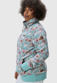 Giacca zip-up floreale in cotone azzurro chiaro con motivi di fiori rosa e verdi. Presenta colletto alto, polsini a coste e accentuazione del logo.