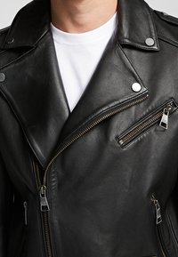 Svart lädermotorcykeljacka med silverdetaljer, som har en snodd krage, dragkedjefickor och en mjuk textur.