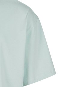 Détail du tissu d'un T-shirt à manches courtes bleu clair montrant l'ourlet et la couture de l'épaule sur un fond blanc uni.