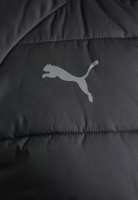 Black padded fabric featuring a subtle gray Puma logo in mid-leap, with visible quilted texture and contrasting stitching details.