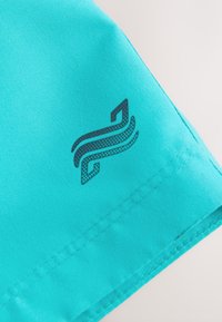 Türkiissinine kangas siledat tekstuuri, millel on varrukal must logo. Saum on korralikult viimistletud.