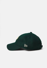 Grön ullbasebollkeps med böjd skärm, med en gul logotyp framtill och en vit varumärkesetikett på sidan.