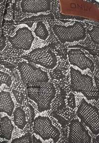 Tecida preta com padrão de cobra branca, apresentando uma etiqueta de couro com a marca "ONLY". Superfície texturizada e detalhes de bolso funcionais.