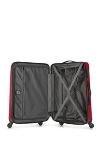 Maleta roja de carcasa dura con acentos negros, cierre de cremallera, interior suave, correas cruzadas para asegurar los objetos, montada sobre cuatro ruedas giratorias.