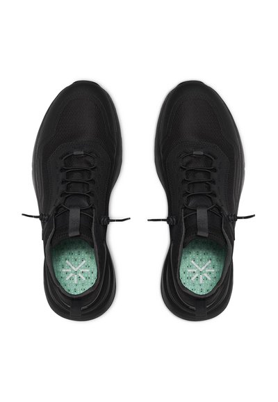 Svarta sportskor med ett meshintryck, med rundad tå, flexibel sula och en mintgrön innersula med ett prickigt mönster.