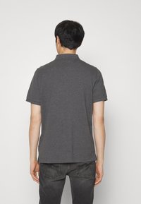 Grå polo skjorte med en folded krave, korte ærmer og en lige kant. Bæret med mørkfarget jeans, der viser en glat stoftekstur.