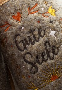 Felt product with brown and grey tones; features colorful embroidery of flowers, hearts, and the text "Gute Seele" in a decorative font.