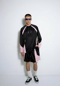 Czarna sportowa koszulka z różowymi akcentami, z długimi rękawami i logo. Pasujące czarne szorty z różowymi detalami, z kieszeniami oraz sportowe sneakersy.