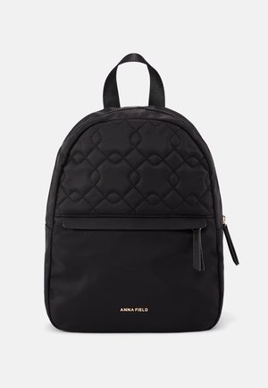 Schwarzer Rucksack mit gestepptem oberen Bereich, Frontreißverschlusstasche, Tragegriff oben und goldfarbenem "ANNA FIELD"-Logo auf der unteren Vorderseite.