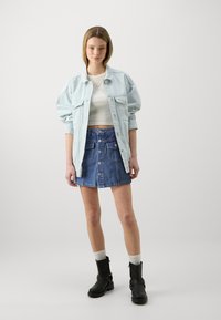 Svijetloplava oversized traper jakna, bijeli skraćeni top, tamnoplava traper suknja s prednjim gumbima i crne ancle čizme s kopčama.