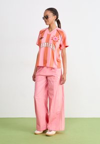 Jersey de manga corta a rayas rosas con detalle floral, combinado con pantalones holgados rosas con rayas laterales. La modelo lleva gafas de sol.
