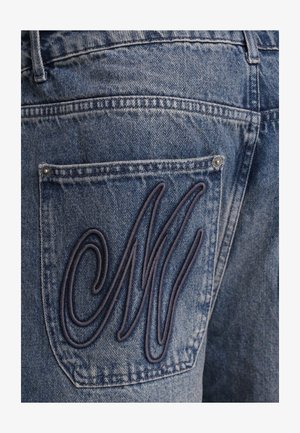 Jeans in denim con una lettera "M" ricamata di colore blu scuro sulla tasca posteriore, con un classico design a cinque tasche e una finitura blu medio.