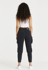 Pantalones cargo negros con bolsillos laterales, diseño ajustado y dobladillos acampanados. Combinados con un top corto blanco y zapatillas blancas.